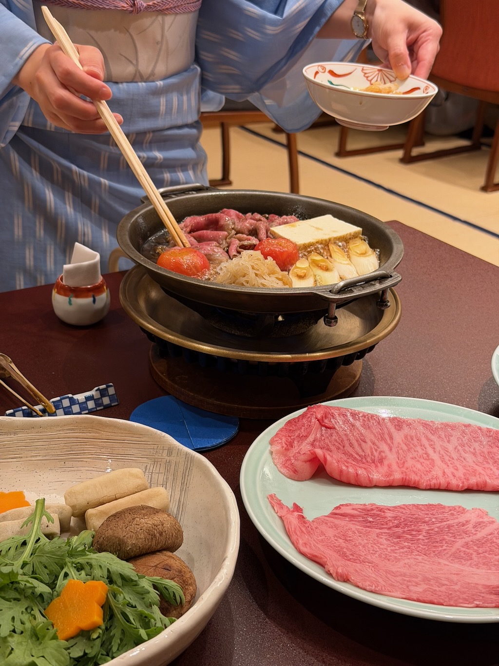 鍋中烹著兩種肥瘦不同的和牛、豆腐與蔬菜，一旁是盛盤的生牛肉片
