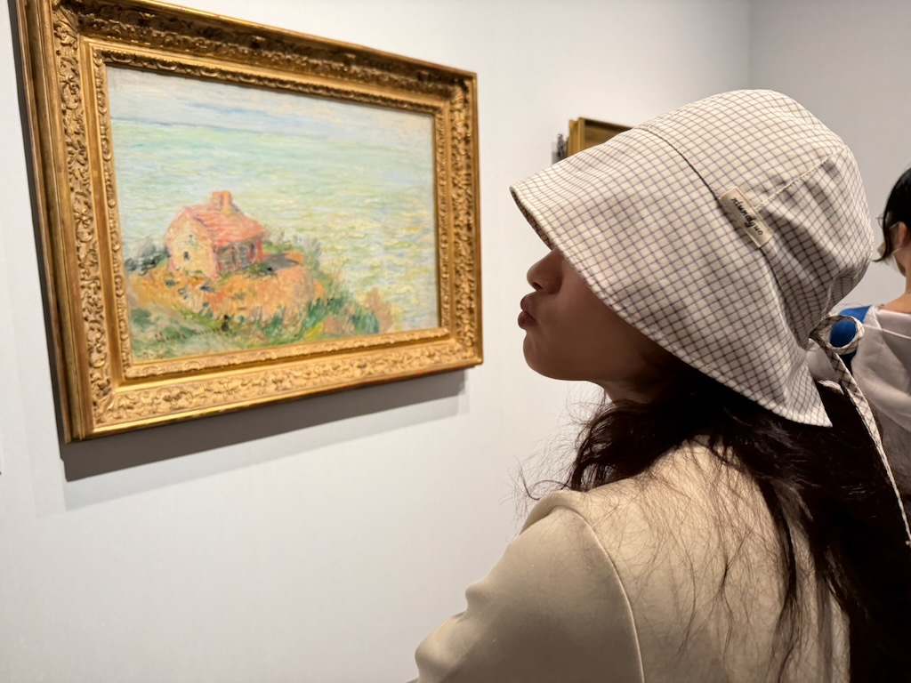 yc 戴著格紋帽，在 Artizon Museum 端詳一幅莫內的海邊小屋畫作